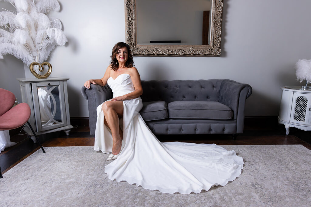 Bride on couch in Stoney Ridge Villa's bridal suite with wedding dress train beautifully on floor during bridal portraits