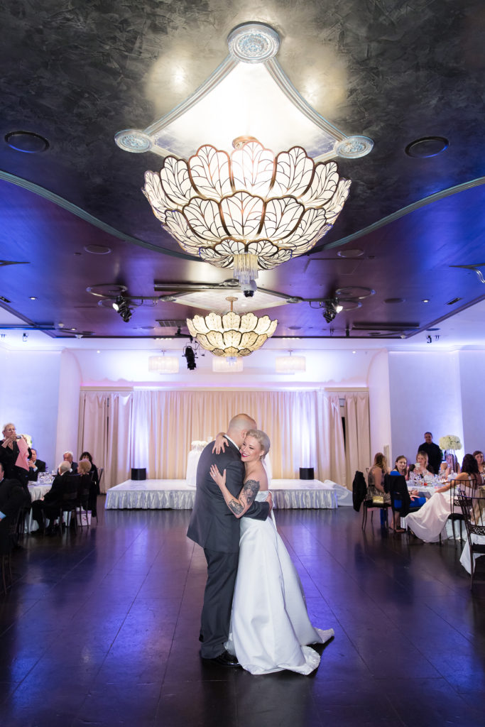dallas wedding photographer captures bride and groom on the dance floor with a chandelier over head and their guests watching them
