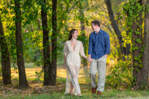 Engaged couple laughing at each other and holding hands while they walk through a golden forest in Colleyville Nature Center
