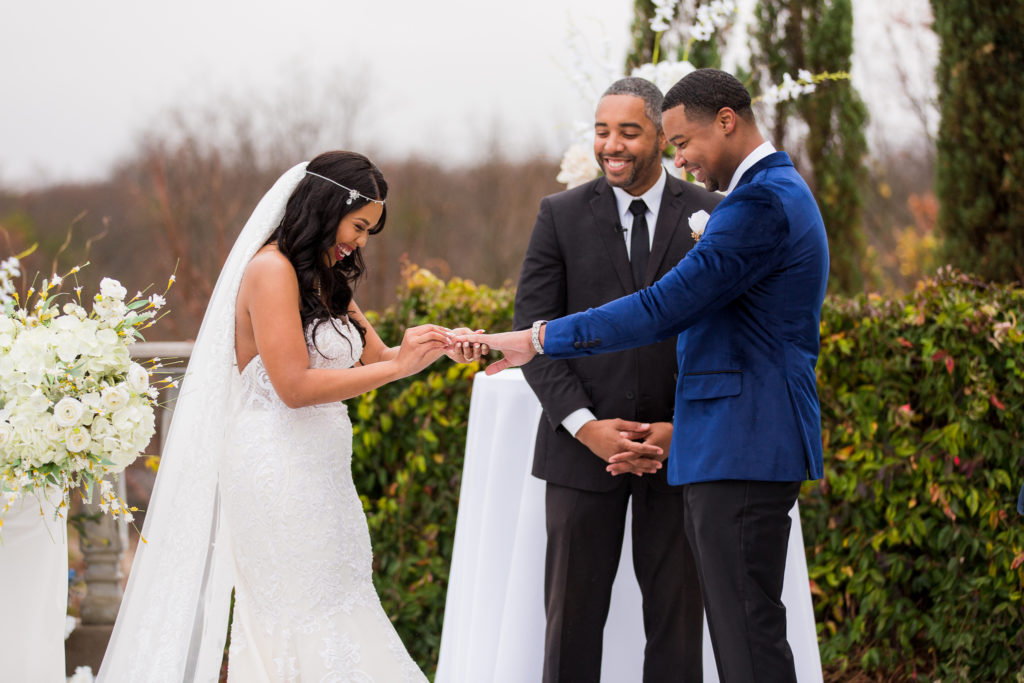 Bride putting ring on grooms hand at their outdoor wedding ceremony during their Dallas weddings