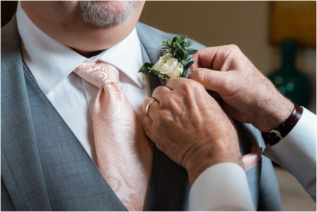 Dallas wedding photographers zoom in on groom's small boutonniere with white roses and greenery