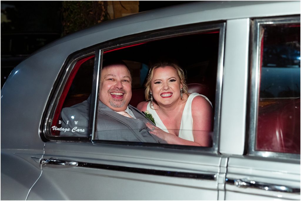 Dallas wedding photographers capture bride and groom grinning through an open window in the back of a vintage silver car