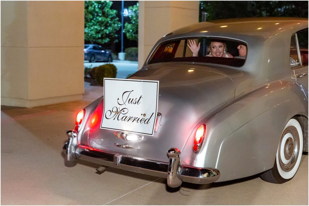 Dallas wedding photographers capture the bride waving out the window of silver car with a sign reading "Just Married"