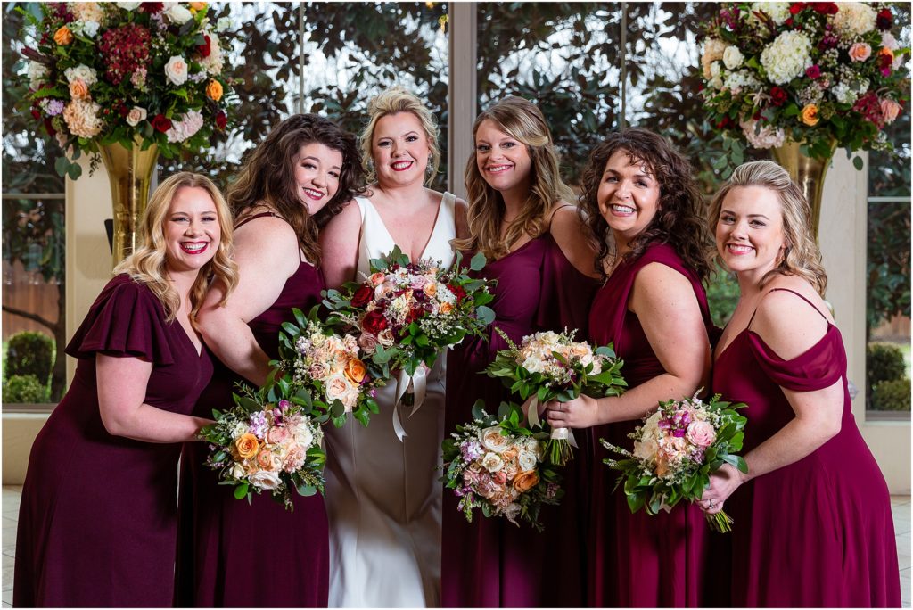 Dallas wedding photographer captures bride with her bridesmaids who are in burgundy bridesmaids dresses holding bouquets together