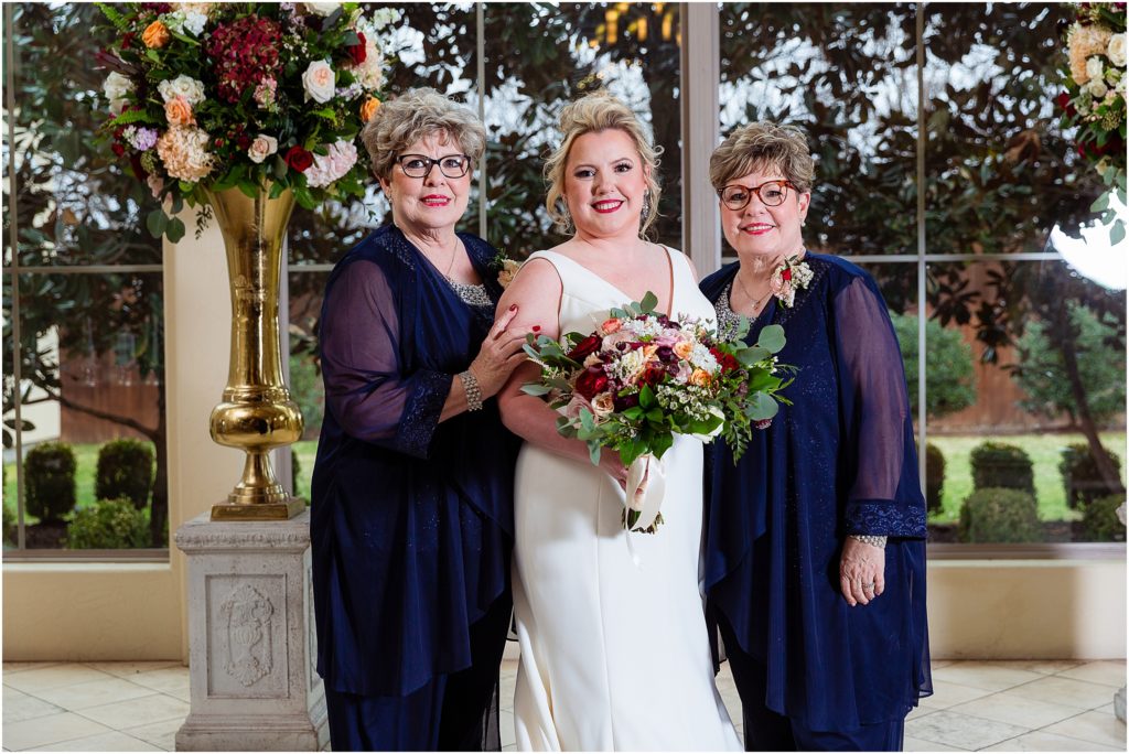 The bride stands with mothers in blue gowns, posing for Dallas wedding photographers