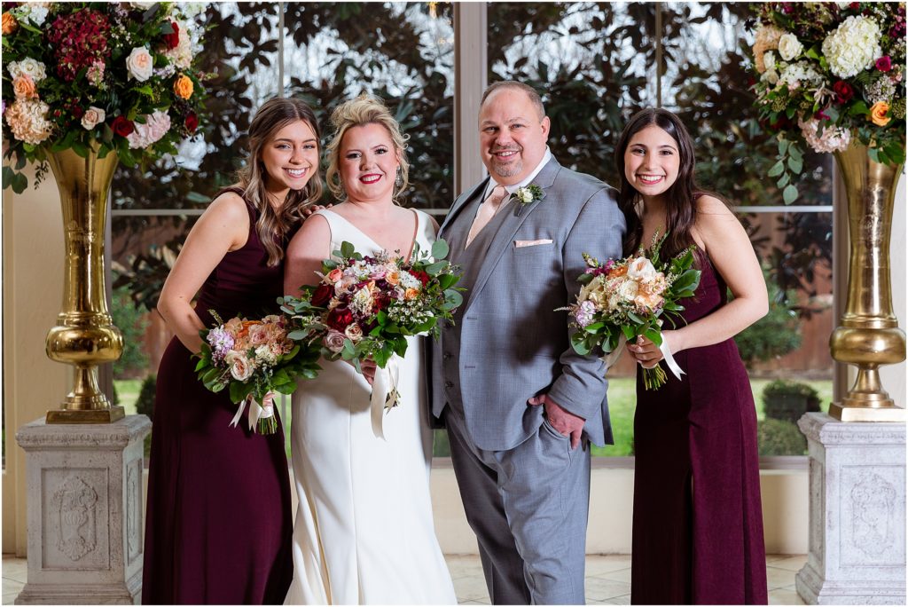 The happy couple with groom's daughters in front of floral arrangements pose for Dallas wedding photographers