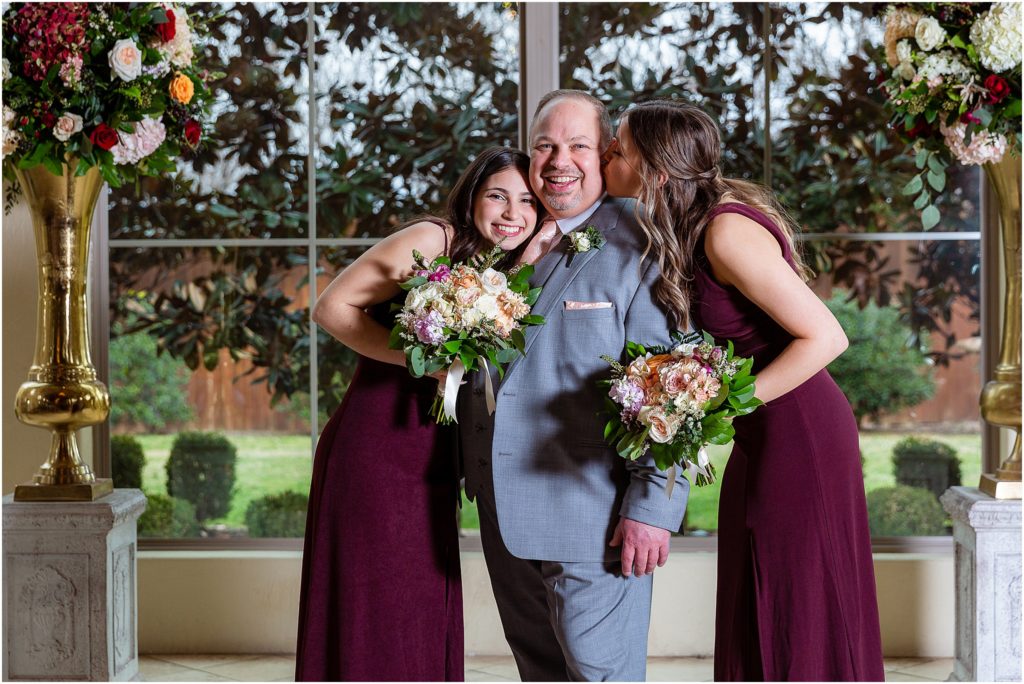 Groom gets kissed and hugged by daughters on either side posing for Dallas wedding photographers