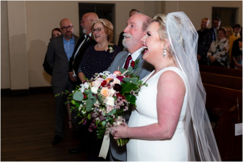 The bride and her father smile as the father gives her away at the altar captured by Dallas wedding photographers