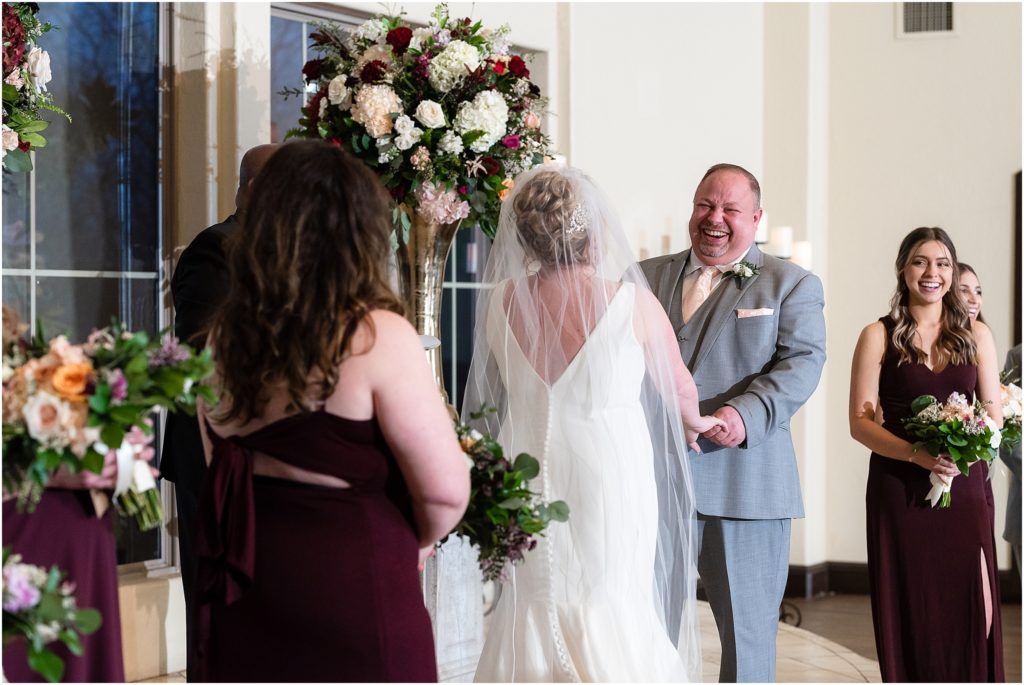 Groom holds brides hands and laughs during ceremony in The Colony wedding venue photographed by Dallas wedding photographers