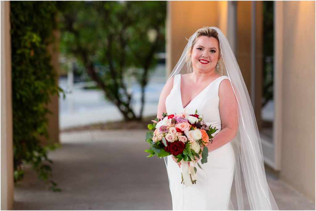 The bride stands slightly off center of the photo with her bouquet covering her hands at a Dallas wedding venue captured by Dallas wedding photographers
