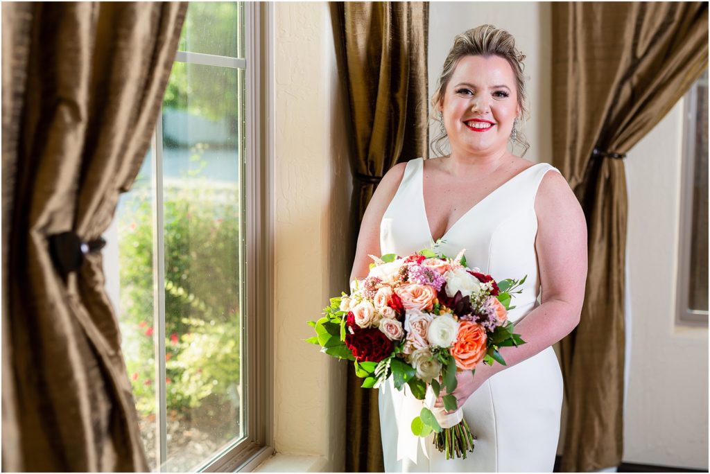 Bride Callie smiles in front of a large window at The Colony, a luxury Dallas wedding venue captured by Dallas wedding photographers