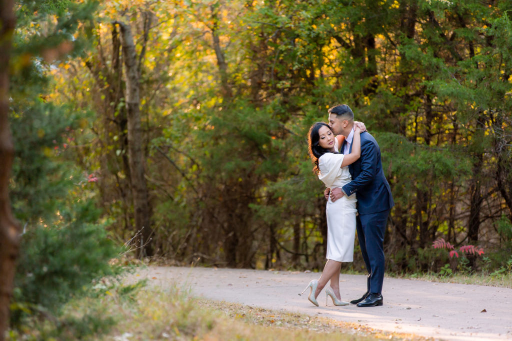 Engaged man kissing woman's temple on a dirt path in the woods