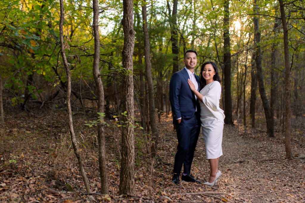 Engaged man and woman standing in the woods together with the woman holding her hand on the mans chest during a Plano park engagement session