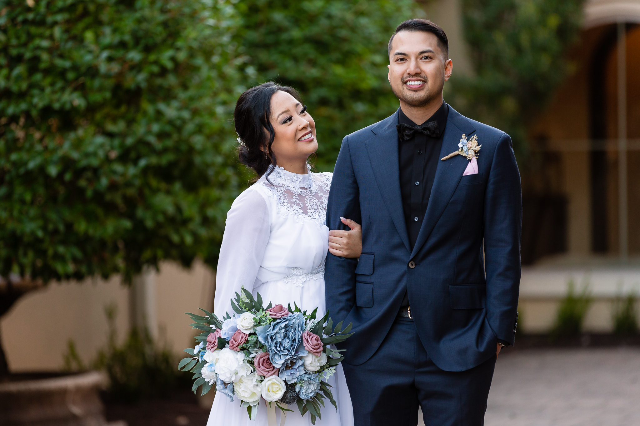 Dallas wedding photographer captures bride holding her grooms arm and smiling up at him while he holds his hands in his pockets for their outdoor wedding portraits