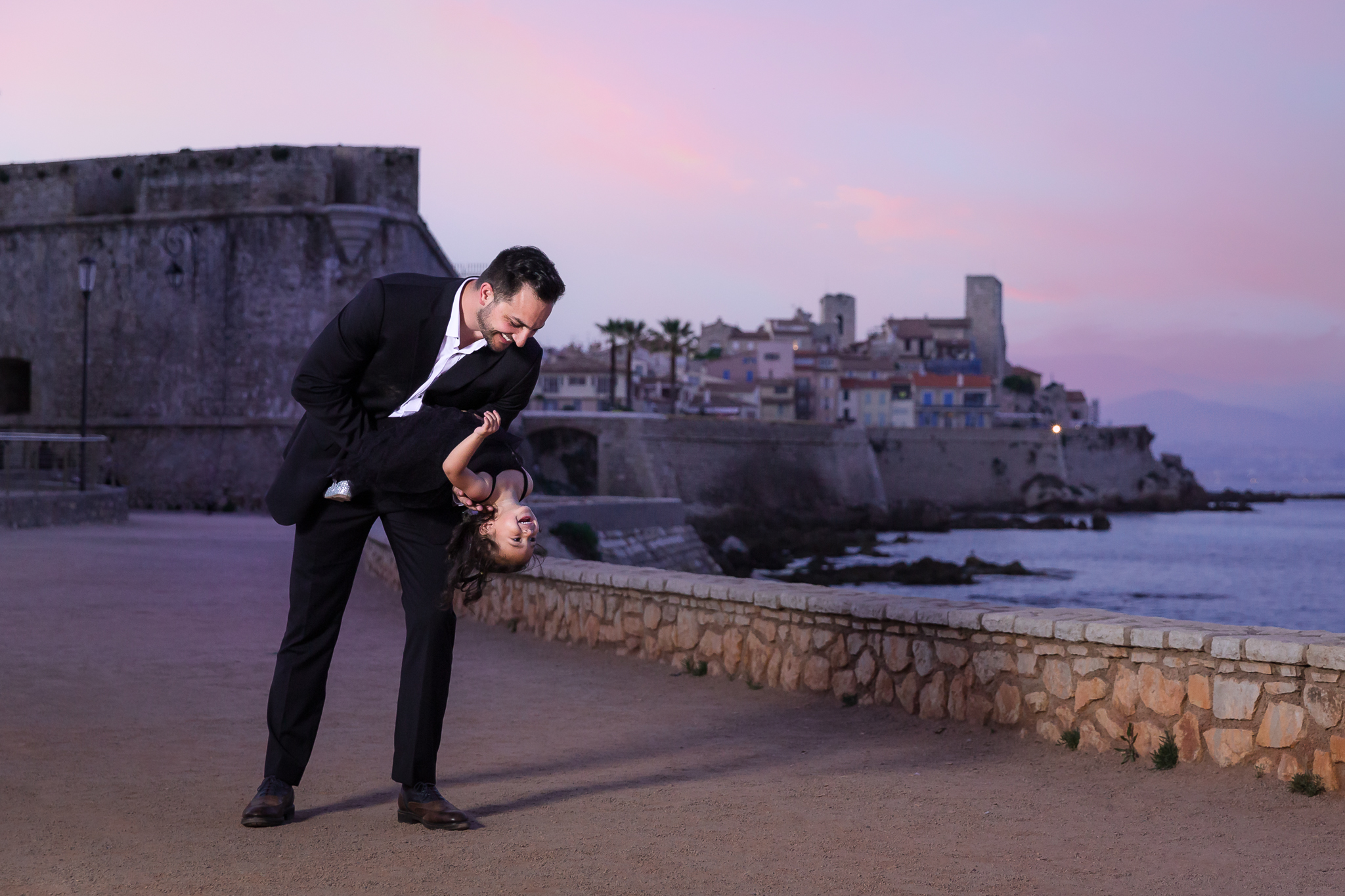 Dad dipping daughter while laughing during family session in Antibes France at sunset