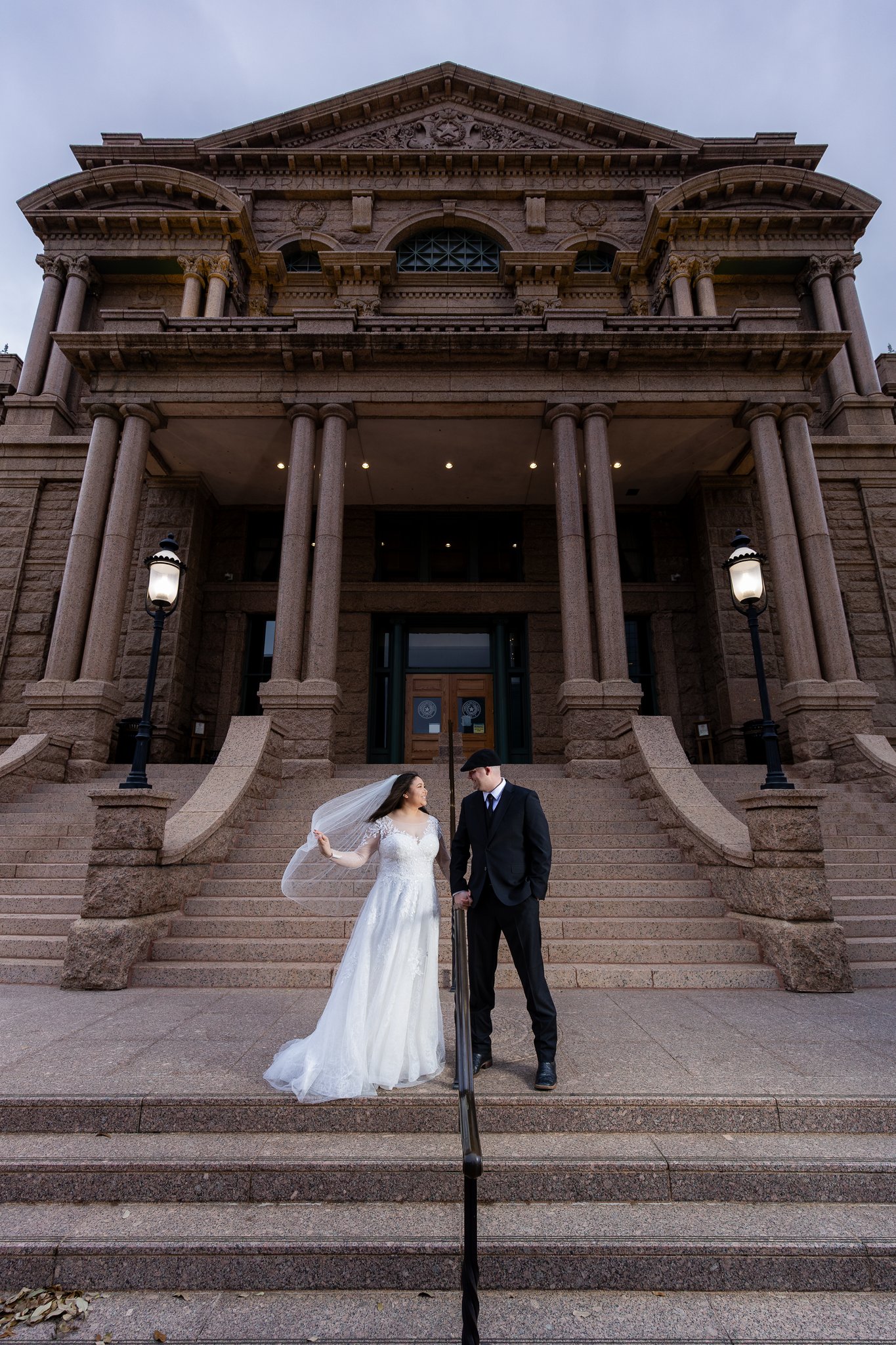 Wedding couple standing hand in hand in front of stairs of the Tarrant County Courthouse in downtown Fort Worth