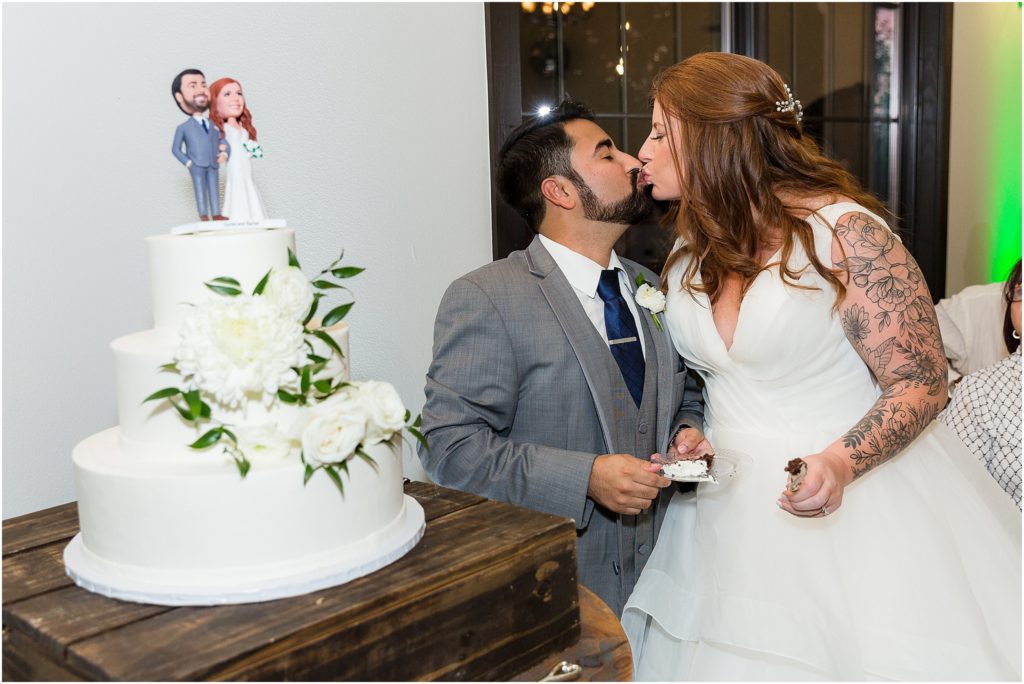 bride and groom cutting their white wedding cake together and kissing at the same time during their indoor wedding reception