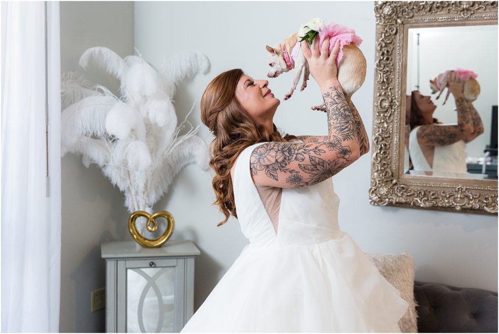 Bride lifting dog up to give nose kisses in wedding dress in Bridal Suite of Stoney Ridge Villa wedding venue