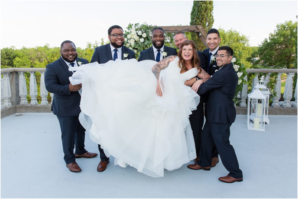 groomsmen carry the bride as they all laugh together while on an outdoor patio at Stoney Ridge Villa captured by Dallas wedding photographers