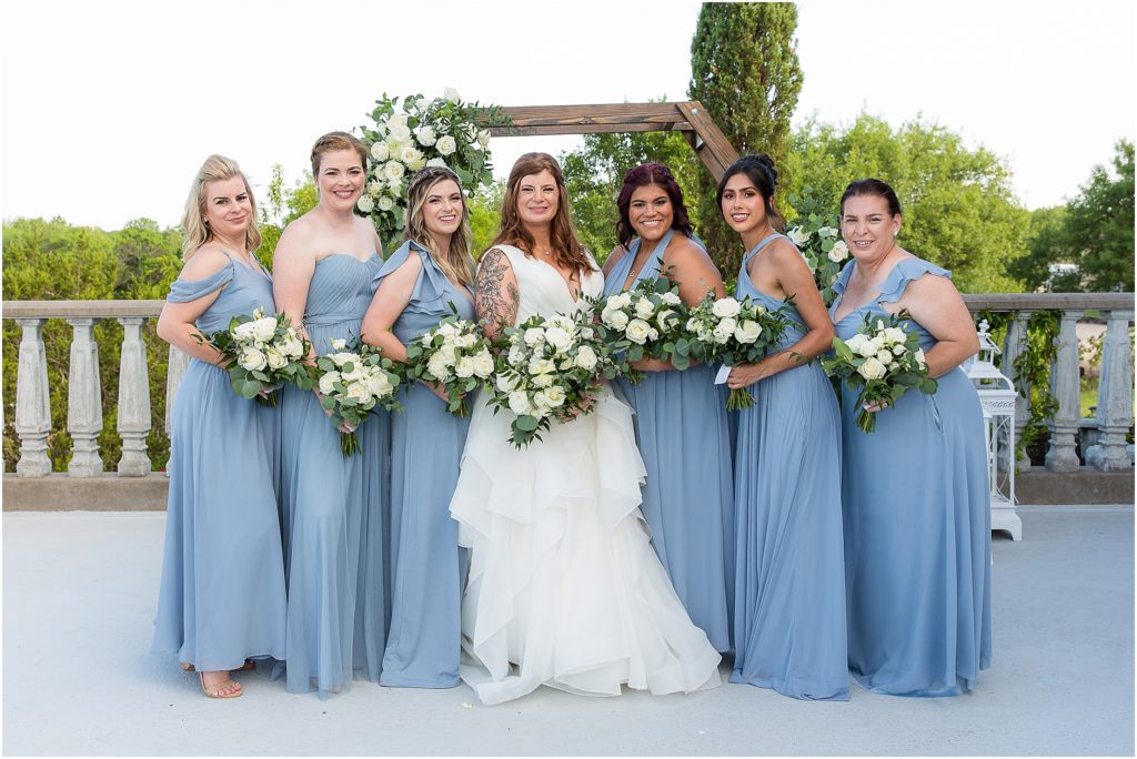 bride and bridesmaids in dusty blue dresses standing on an outdoor patio at Stoney Ridge Villa captured by Dallas wedding photographers