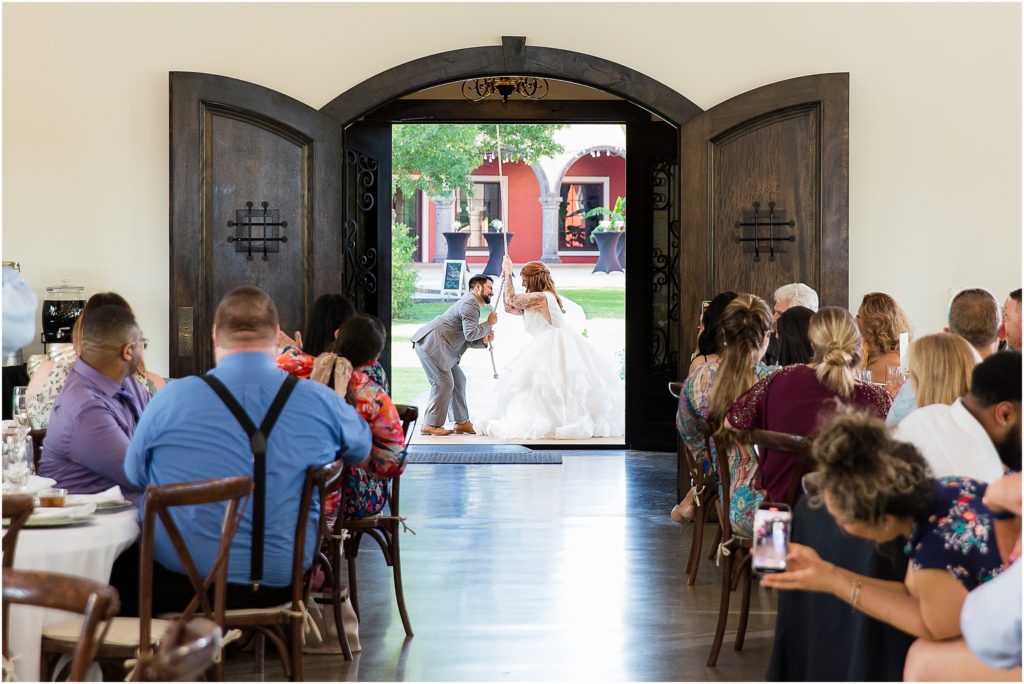 bride and groom exiting their wedding ceremony and ringing a large bell as they leave while their wedding guests watch them