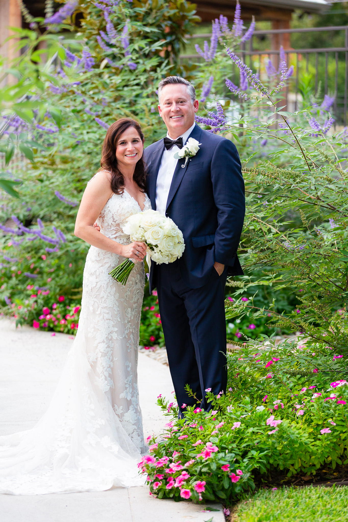 Granbury wedding with bride and groom in a garden together for their outdoor wedding with bride in a lace wedding dress holding a large rose bouquet