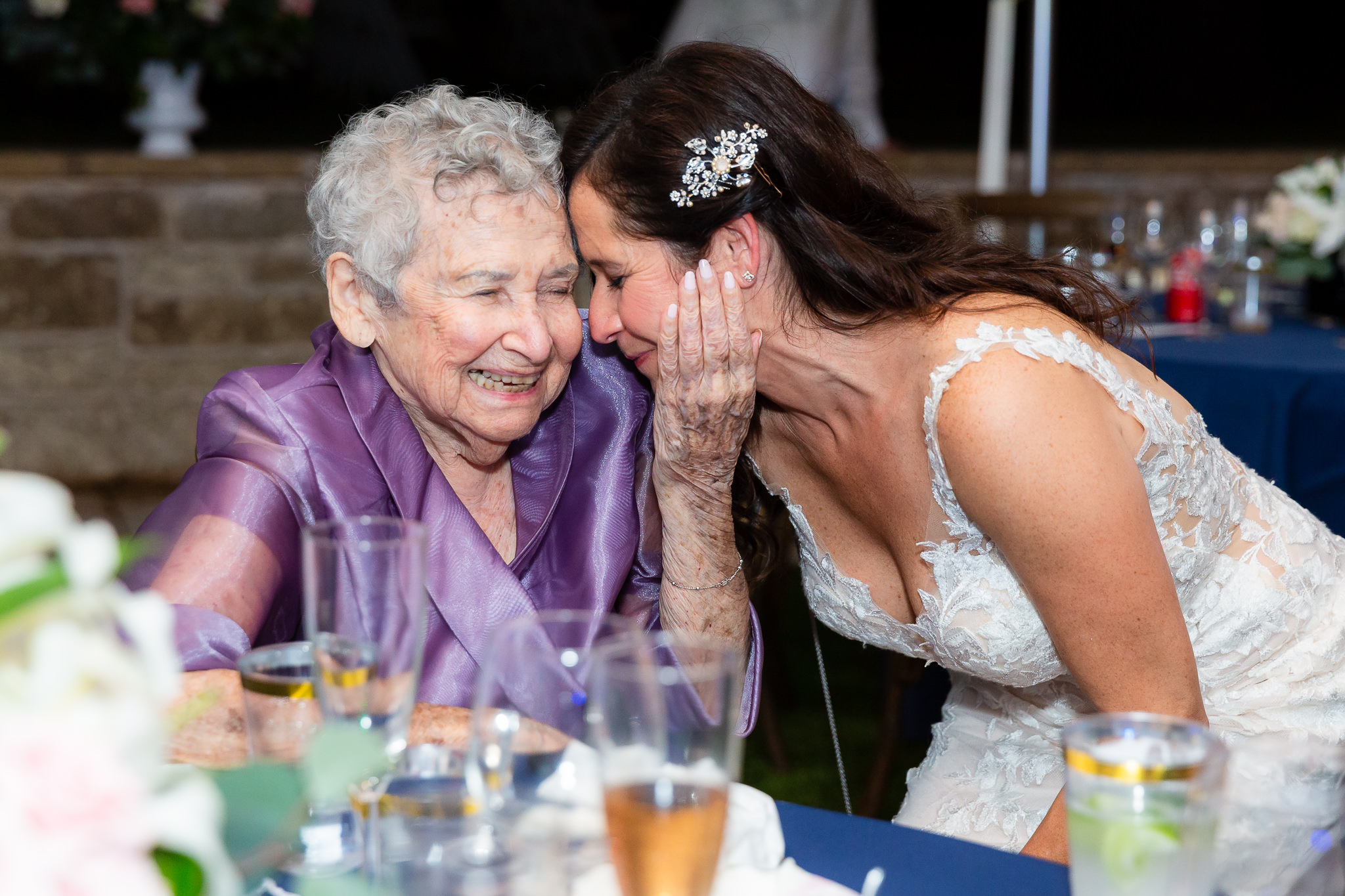 bride leaning down to talk with her grandmother as the grandmother holds the brides cheek and laughs during the Granbury wedding reception