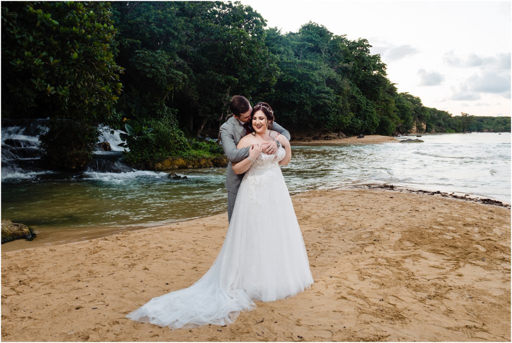 dallas wedding photographer captures destination wedding with bride and groom hugging each other with the groom standing behind the bride and holding her shoulders as she looks back to him