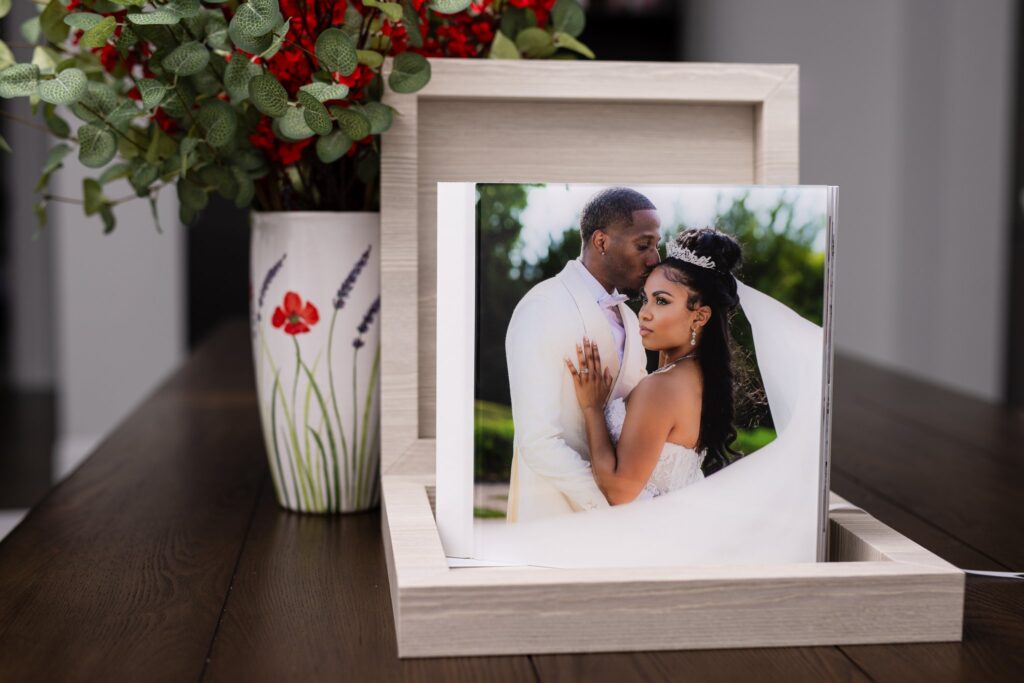 an heirloom wedding album with white spine and an acrylic photo cover of groom kissing bride on the temple during wedding at knotting hill place venue standing up inside of an open luxury light colored wooden box