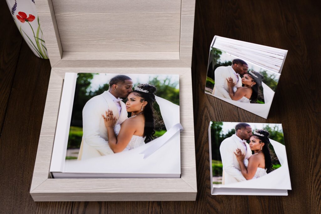 an heirloom wedding album with white spine and an acrylic photo cover of groom kissing bride on the temple during wedding at knotting hill place venue sitting inside of a luxury wooden box accompanied by two smaller duplicate parent albums with the same image