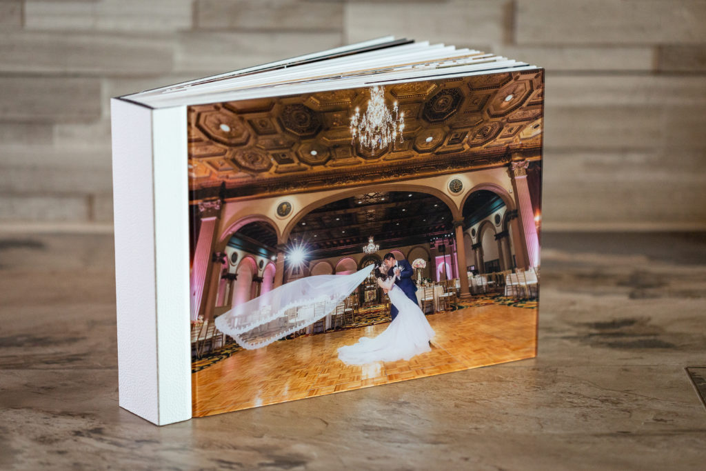 heirloom wedding album with acrylic photo cover of couple doing a dip in an extravagantly elegant hotel ballroom with the bride's veil flying