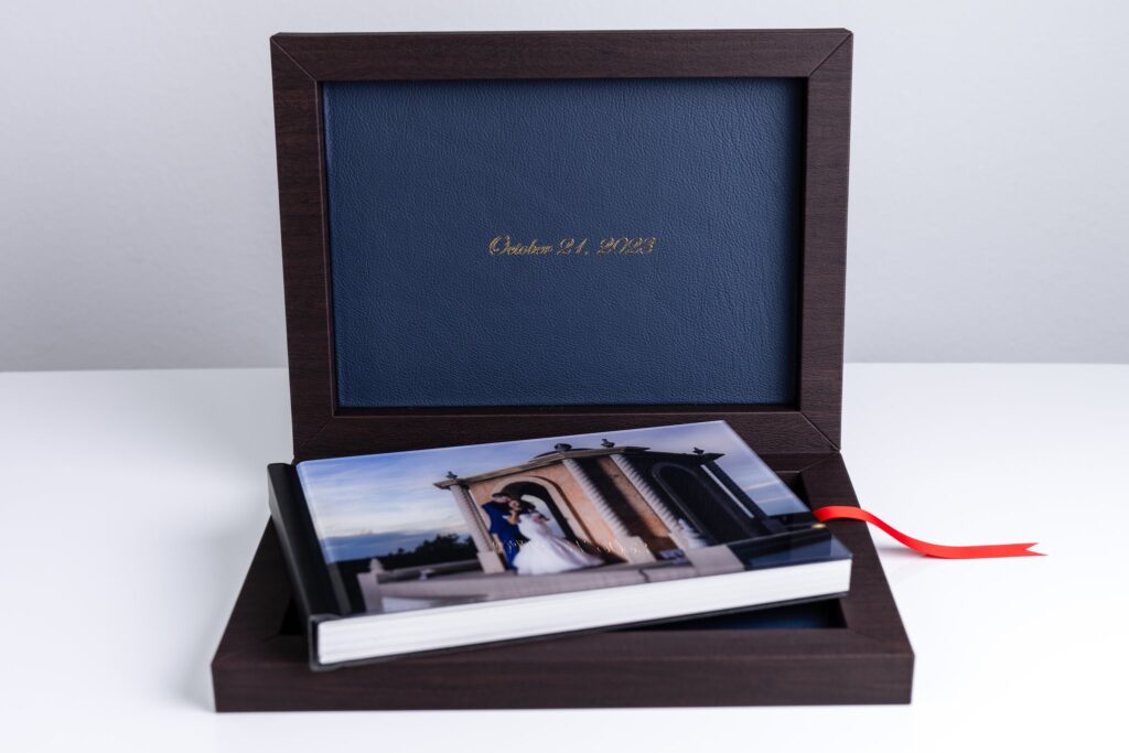 an heirloom wedding album with black spine and an acrylic photo cover of bride and groom hugging on stoney ridge villa wedding venue's rooftop sitting inside of an open luxury dark wood and blue leather box