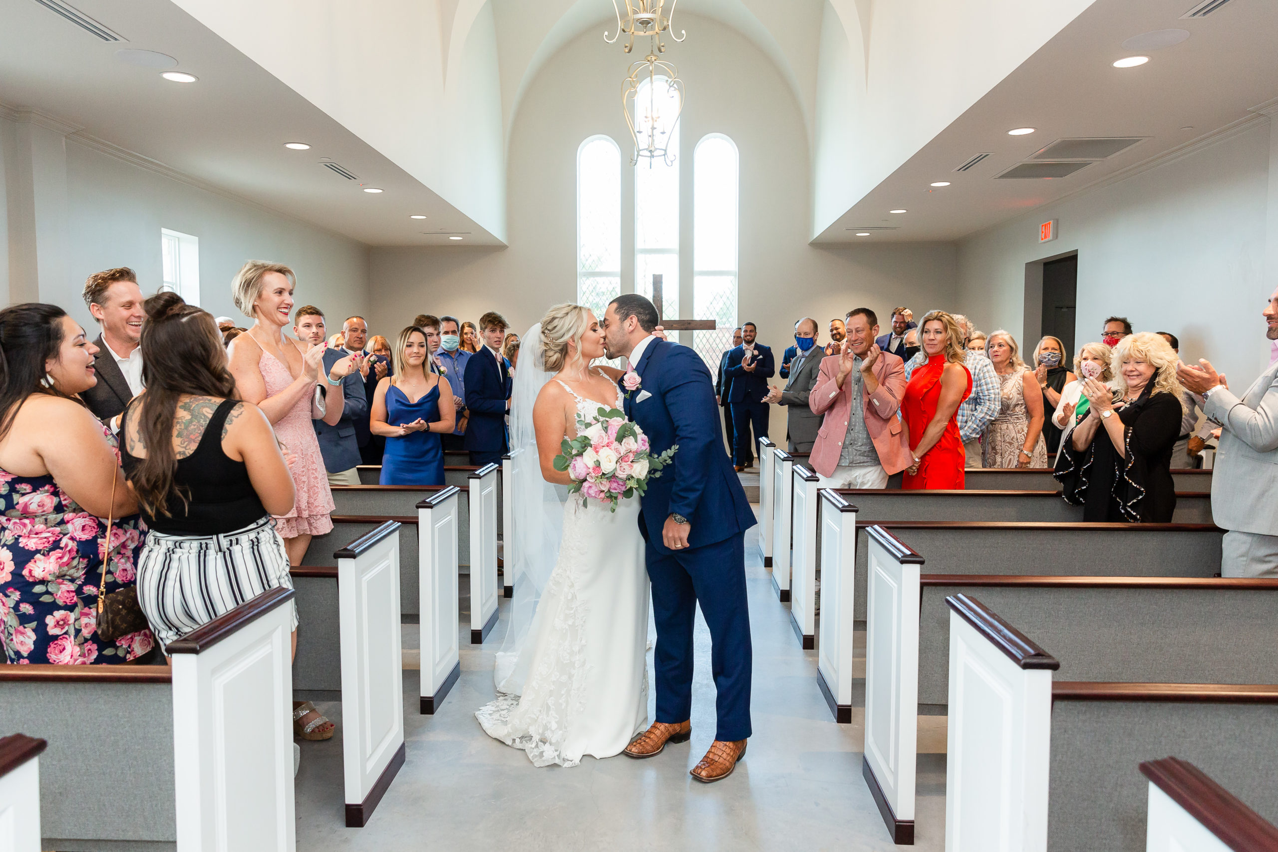 Dallas wedding photographer captures wedding ceremony exit with bride and groom walking down the aisle and kissing while their guest stand and cheer for them
