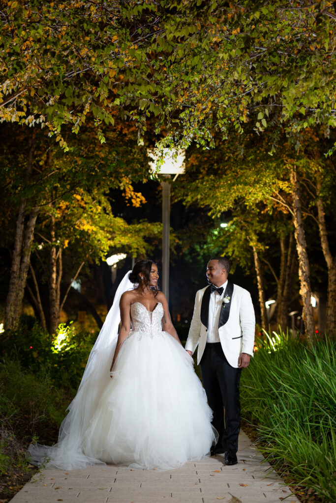 Bride and groom holding hands and walking down a path in a garden at night