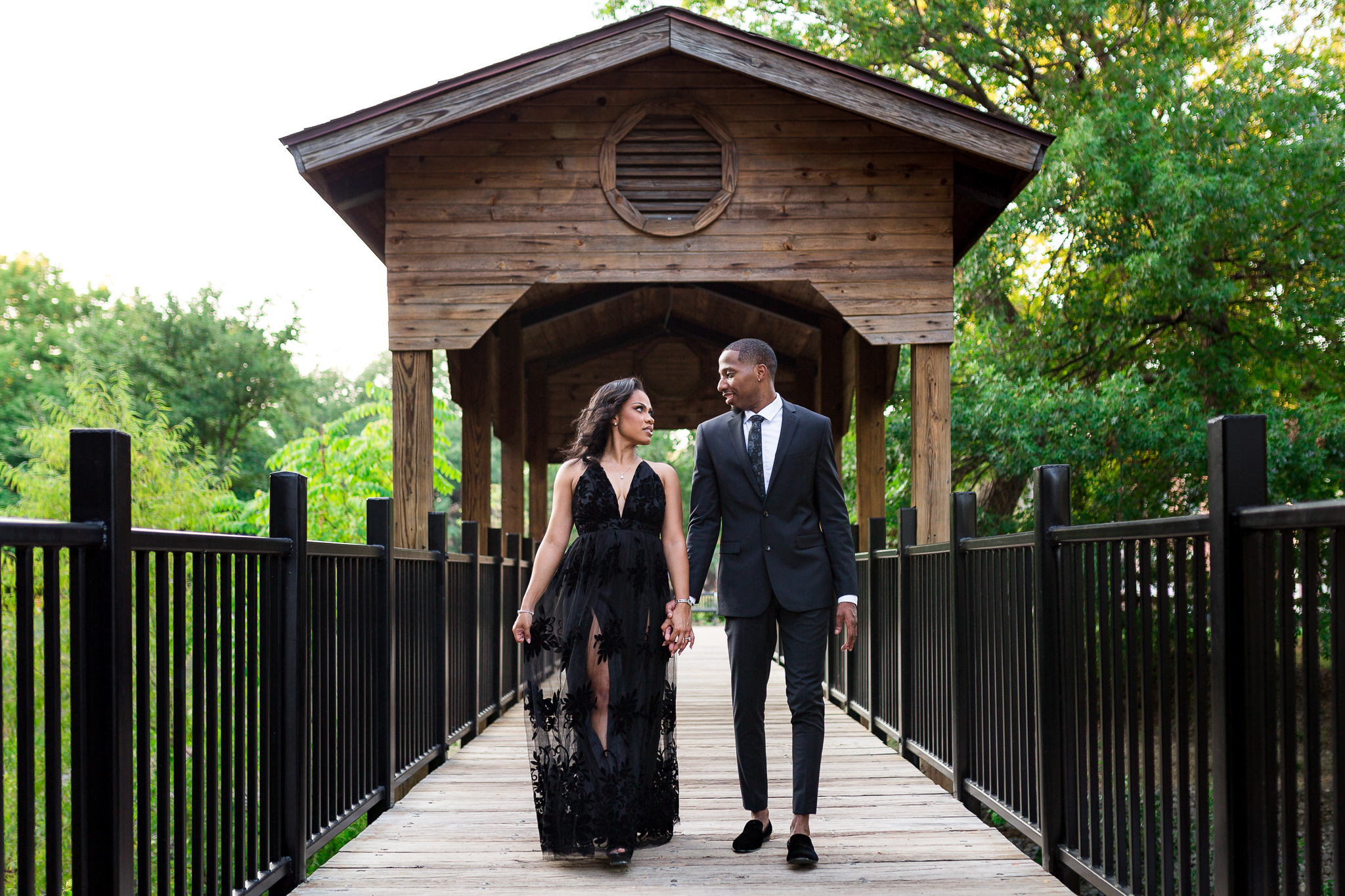 Dallas wedding photographers photographs engagement photos dallas with man and woman holding hands and walking on a bridge together away from a little barn like pergola