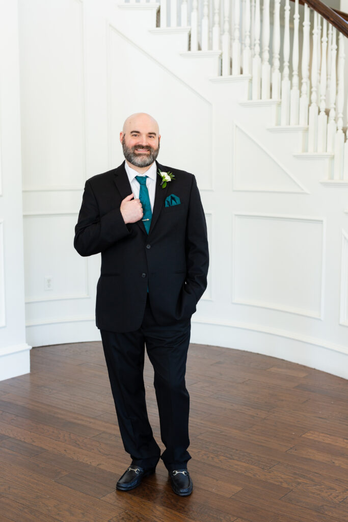Groom in black suit and teal tie during wedding portraits