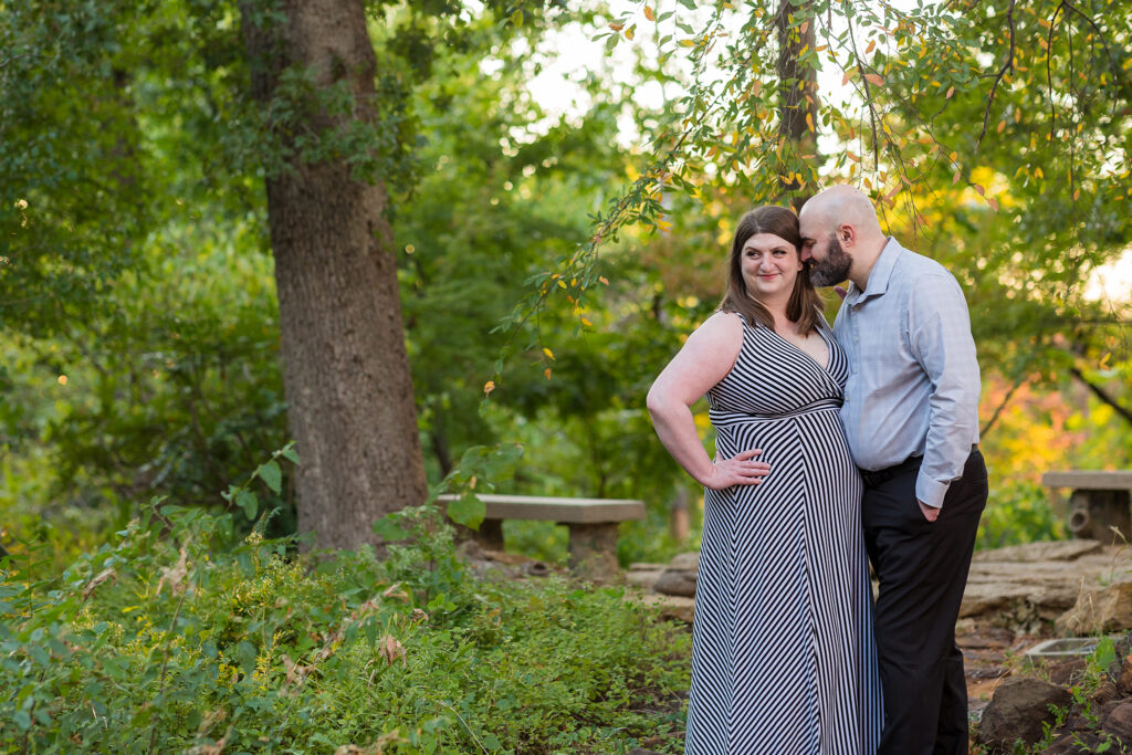 Man nuzzling into his fiancée in a forest with rock pathway and lush trees behind them during engagement session at TWU