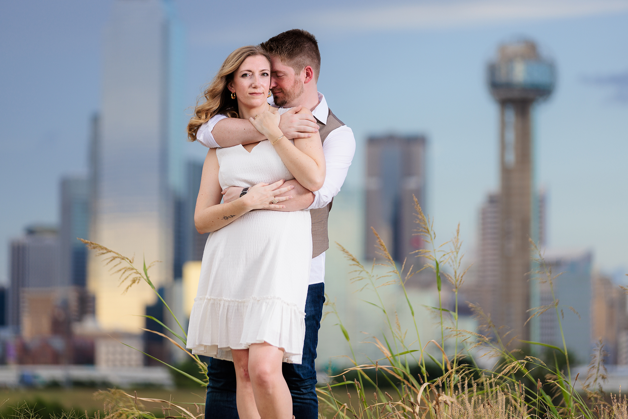 Dallas wedding photographers captures man nuzzling into his fiancee's neck during outdoor engagement session wearing white dress