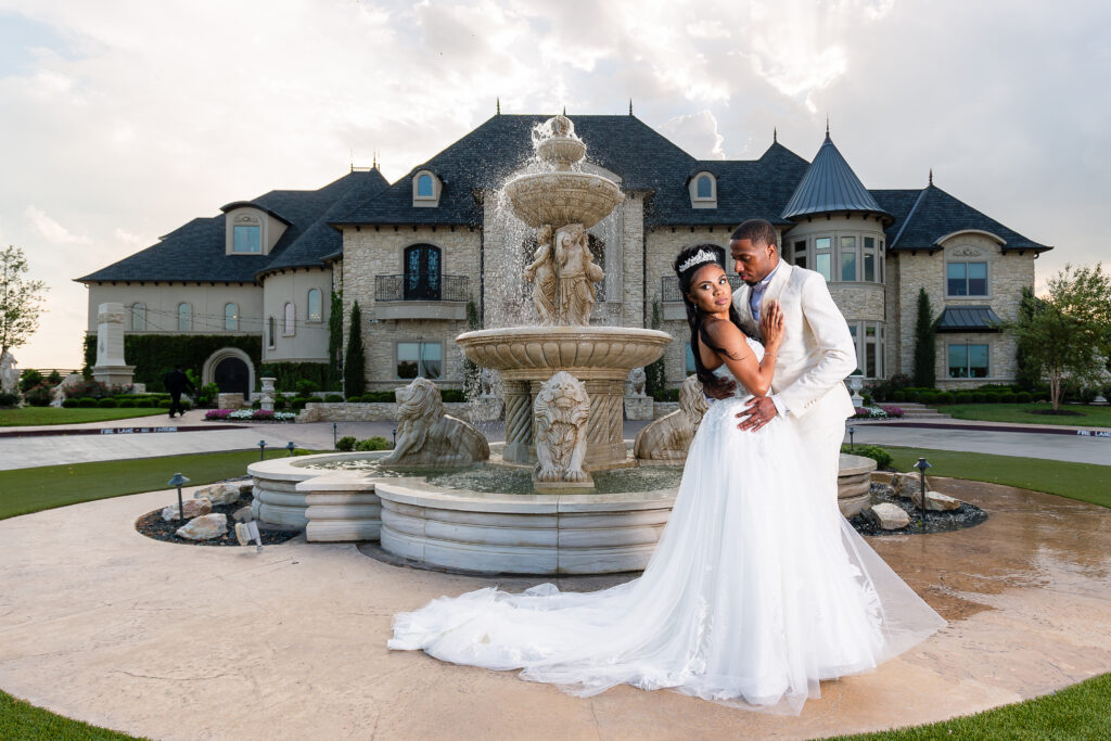 Bride and groom dipping while looking away during bridal portraits in front of fountain at Knotting Hill Place at sunset in Little Elm, TX