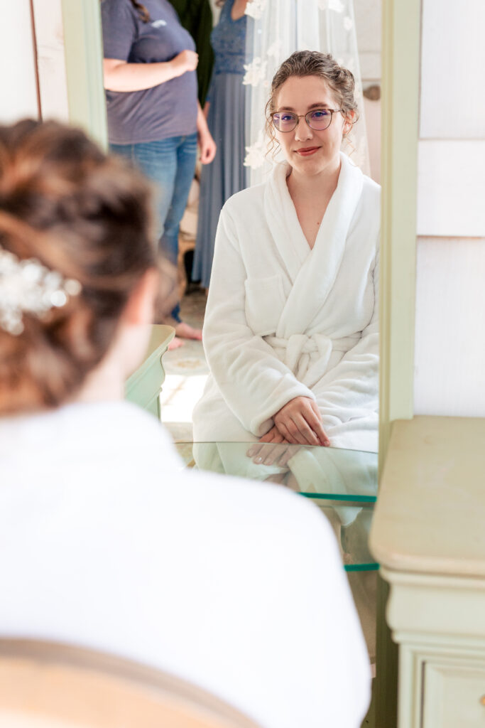 Dallas wedding photographers capture bride sitting on chair in front of mirror getting makeup done before The Big White Barn Wedding