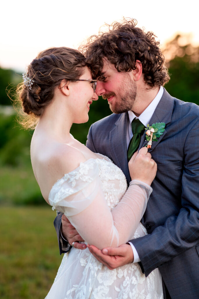 Dallas wedding photographer captures bride and groom embracing in a fiel at dusk with the bride holding her groom suit coat as he leans into her