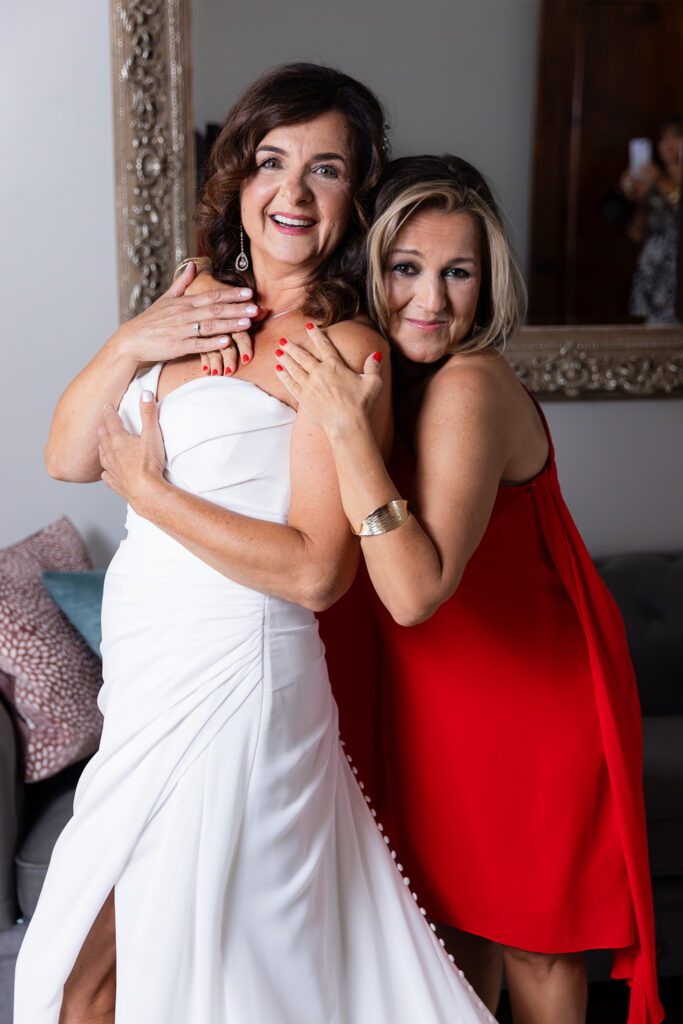 Dallas wedding photographer captures friend hugging bride after zipping up her wedding dress in Stoney Ridge Villa bridal suite