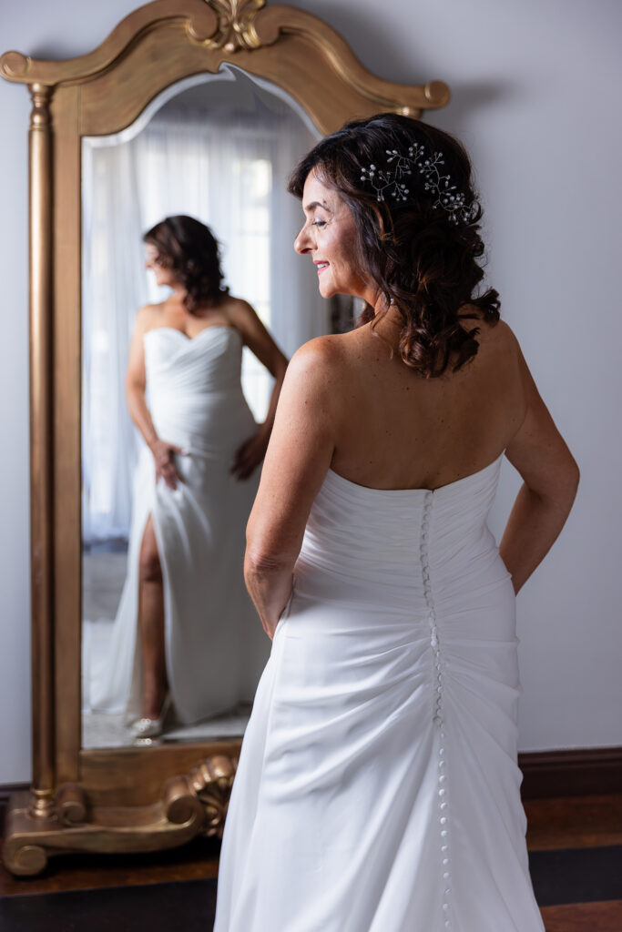 Dallas wedding photographer Stefani Ciotti Photography captures bride and bride's reflection in golden framed mirror in Stoney Ridge Villa's bridal suite in Azle TX