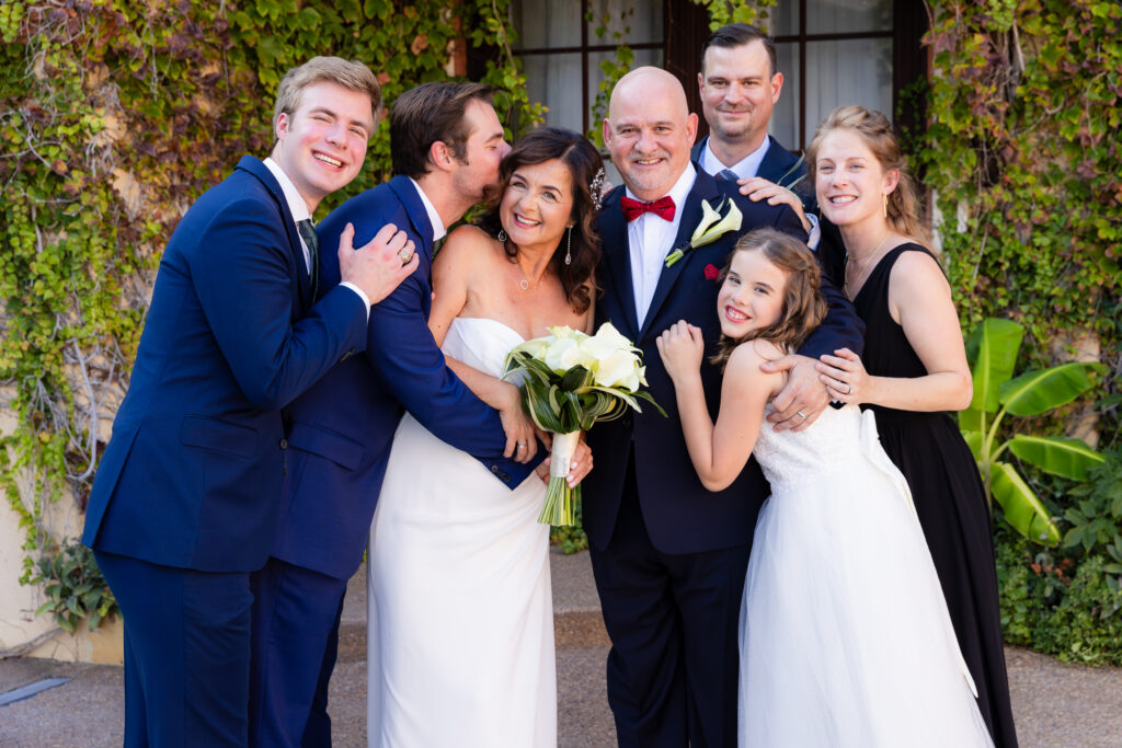 Dallas wedding photographer captures couple standing together smiling with family hugging them at stoney ridge villa in azle texas