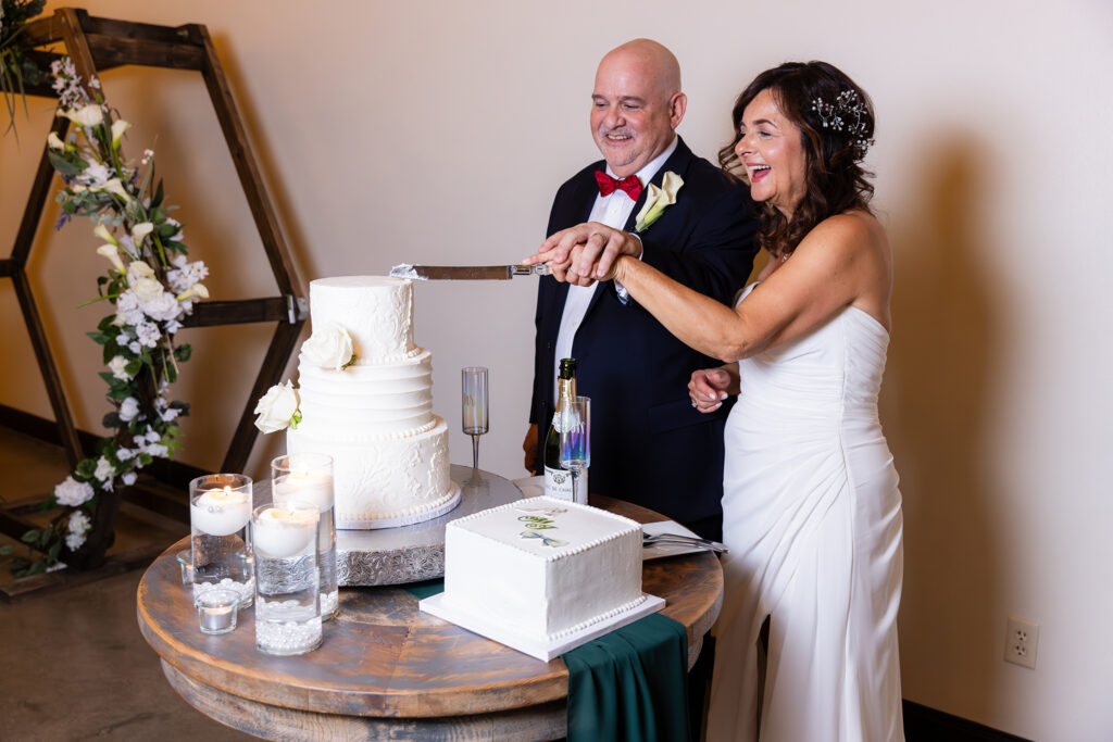 Dallas wedding photographer captures bride and groom laughing while cutting their 3 tiered wedding cake