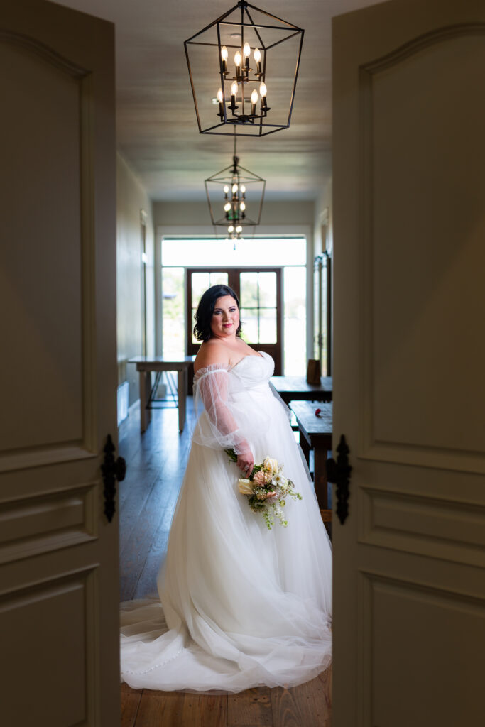 Dallas wedding photographer Stefani Ciotti Photography creatively captures bride wearing wedding gown holding bouquet standing between open doors