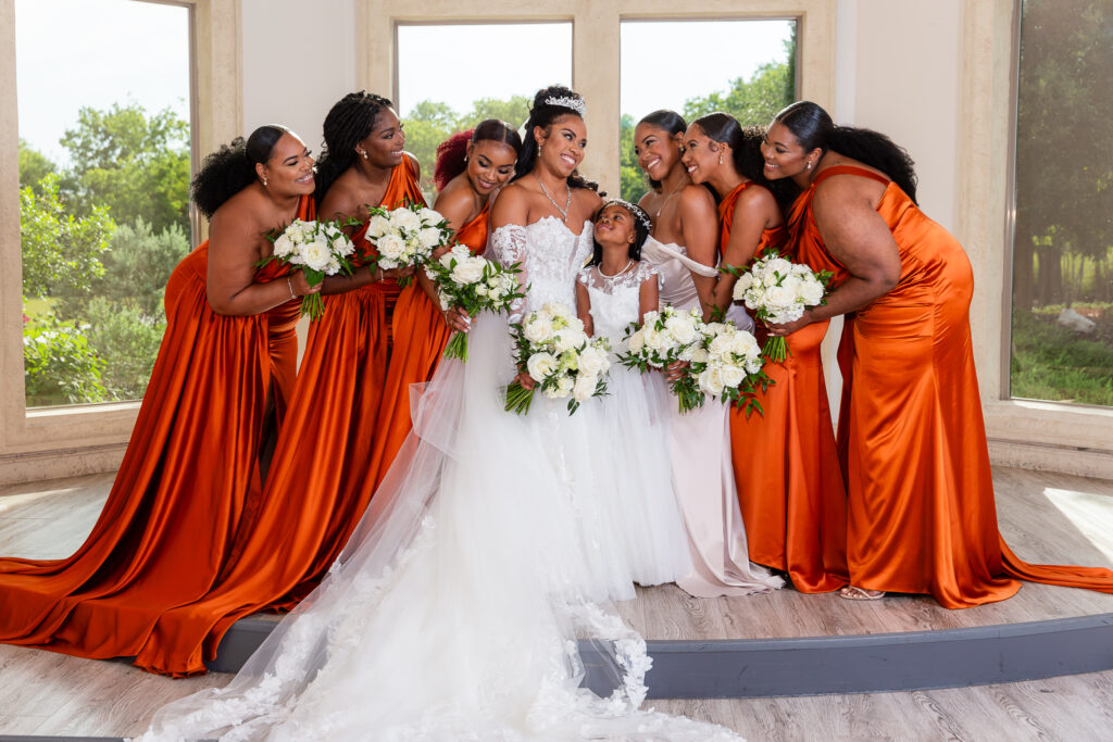 bride with wedding party in orange bridesmaid dresses smiling at each other in knotting hill place wedding venue ceremony cathedral room in little elm texas by dallas wedding photographer Stefani Ciotti Photography