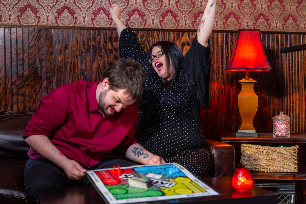 Bride cheering and groom angry playing Sorry board game during engagement session in Deep Ellum Texas