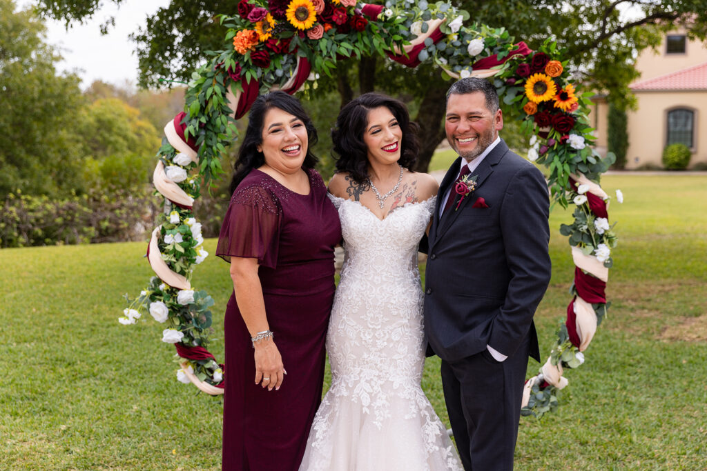 Bride smiling at dad, while dad and mom laugh at camera on lawn at Stoney Ridge Villa wedding venue