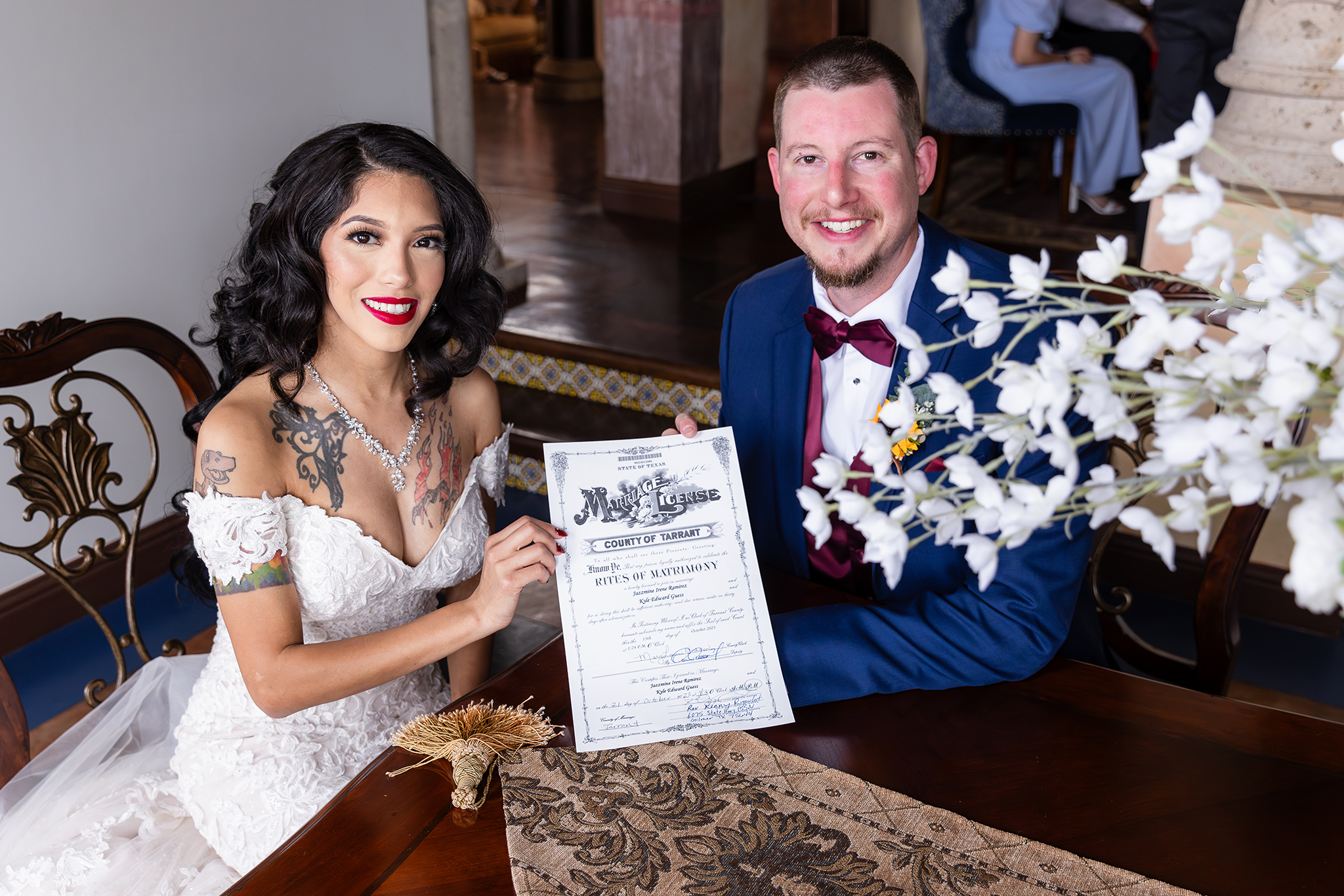 Tattooed bride and groom in navy suit smiling while holding signed marriage license at table in Stoney Ridge Villa wedding venue